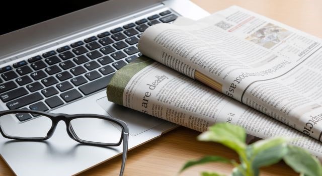 最近のニュースが載っているパソコンと新聞紙